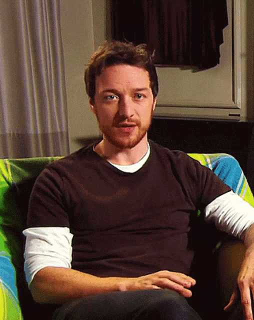 a man with a beard is sitting in a chair with his hands on his knees