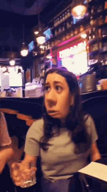 a woman making a funny face while sitting at a table with a glass
