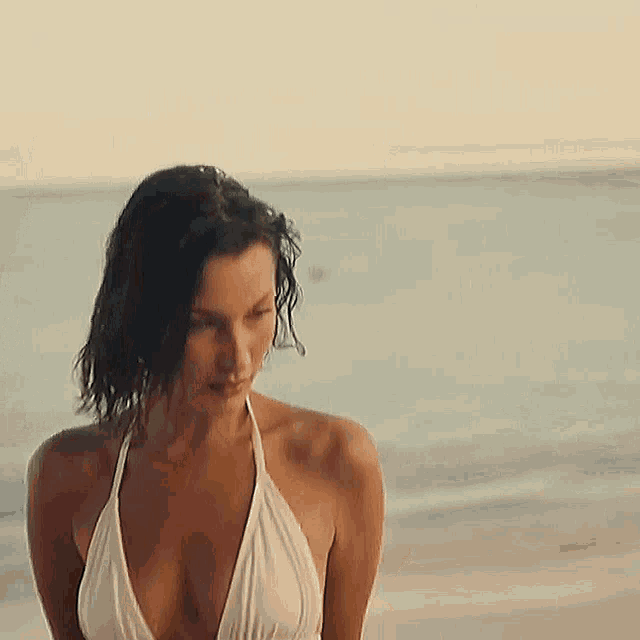 a woman in a white bikini is standing on the beach near the ocean .