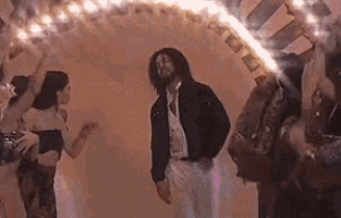 a man with dreadlocks is dancing in front of a crowd of people in a room .