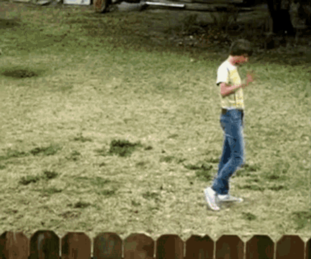 a man in a yellow shirt and blue jeans is walking across a grassy field