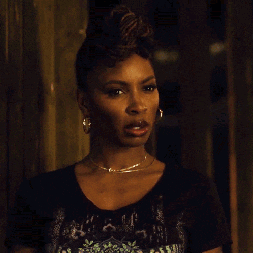 a woman wearing a necklace and hoop earrings looks at the camera with a surprised look on her face