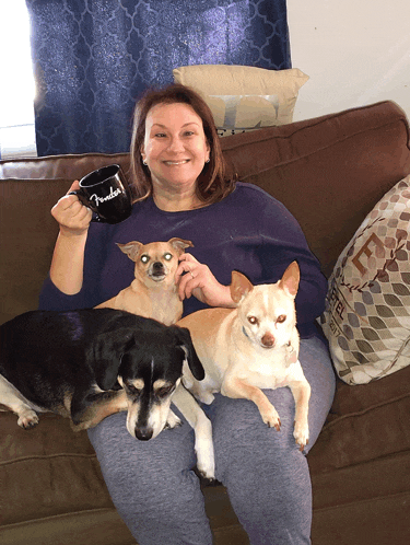 a woman is sitting on a couch with three dogs and holding a mug that says friends