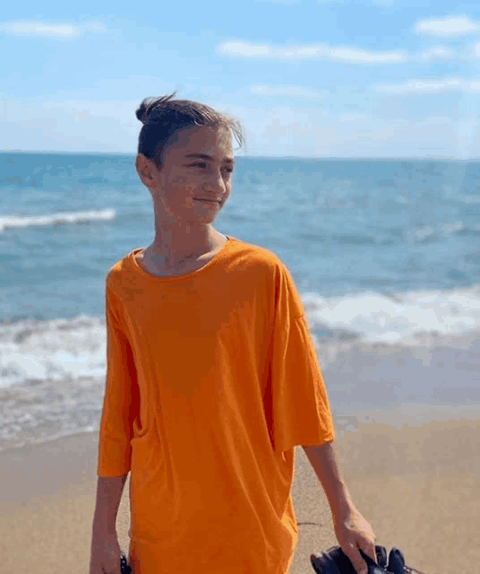 a young boy in an orange shirt is standing on a beach holding a pair of binoculars .