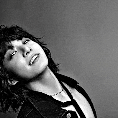a black and white photo of a young man with long hair and a piercing in his lip .