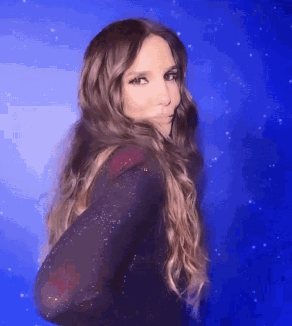 a woman with long brown hair is standing in front of a blue background with stars .