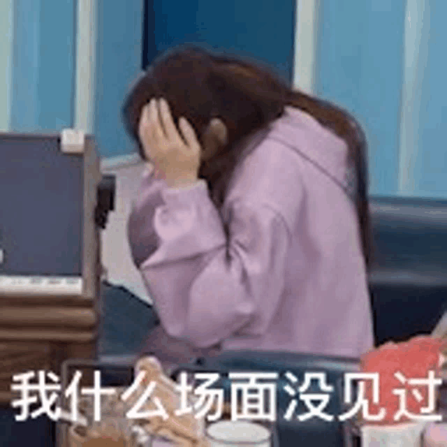 a woman in a purple sweatshirt is covering her face with her hands while sitting on a couch .