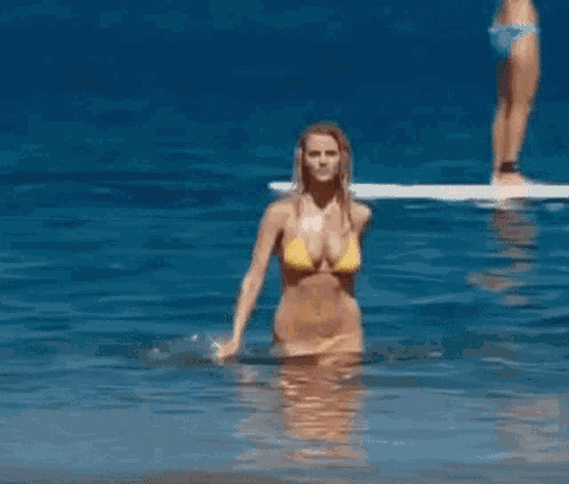 a woman in a yellow bikini is standing on a beach .
