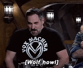 a man wearing a black t-shirt that says `` wolf howl '' is sitting at a table .