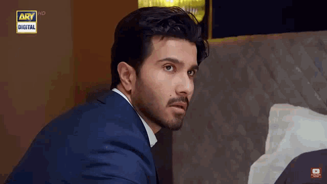 a man in a suit is sitting in front of a bed and a sign that says ary digital on it