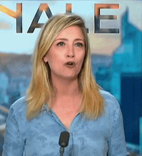a woman in a blue shirt stands in front of a microphone with the word yale in the background