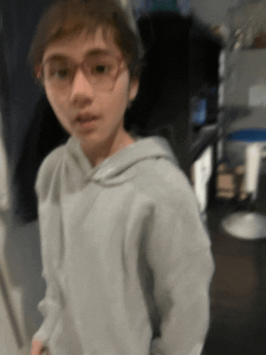 a boy wearing glasses and a grey hoodie