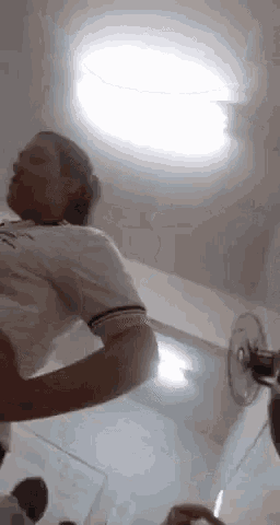 a man in a white shirt is standing in a room with a fan on the wall .