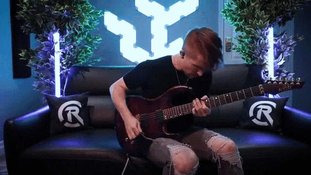 a man playing a guitar on a couch with pillows that say r