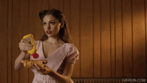 a woman in a pink dress is holding a hot dog and a bottle of mustard in her hand