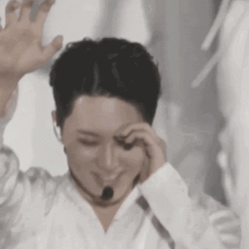 a man in a white shirt with a microphone around his neck is covering his face with his hand .