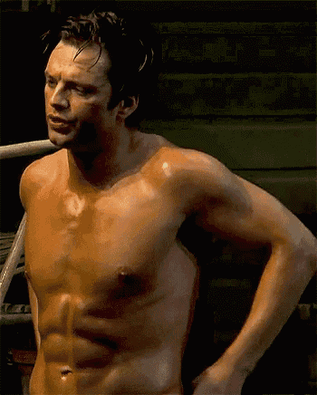 a shirtless man is standing in a dark room with his hands behind his back .