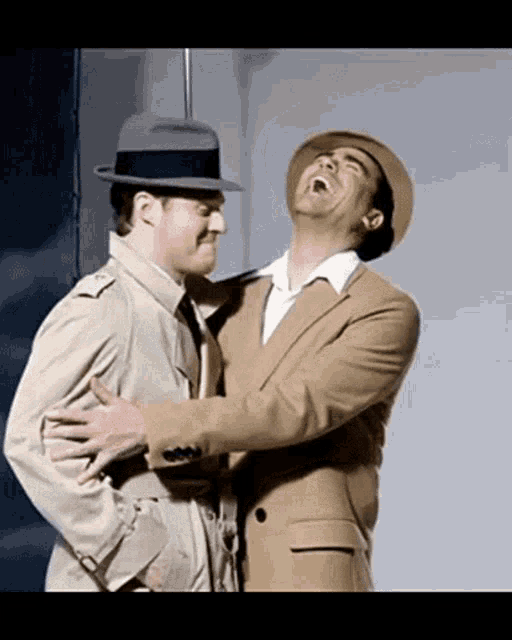 two men in suits and hats are hugging and laughing together