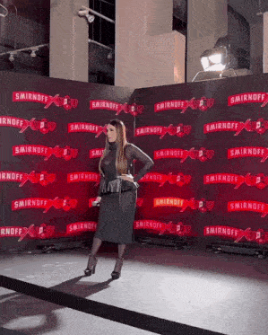 a woman stands in front of a wall that says smirnoff on it