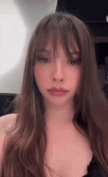 a young woman with long brown hair and bangs is taking a selfie .