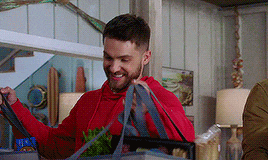 a man in a red hoodie is holding a bag of groceries .
