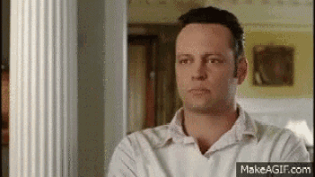 a man in a white shirt is standing in a room with his arms crossed and looking at the camera .