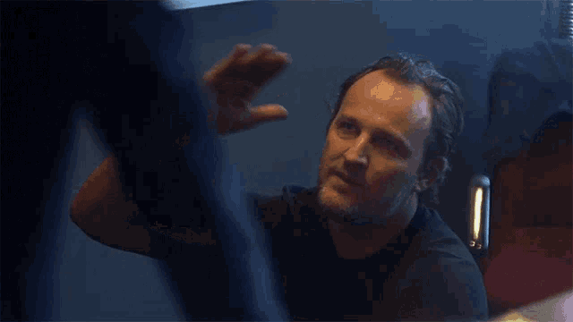 a man with a beard wearing a black shirt is standing in a dark room
