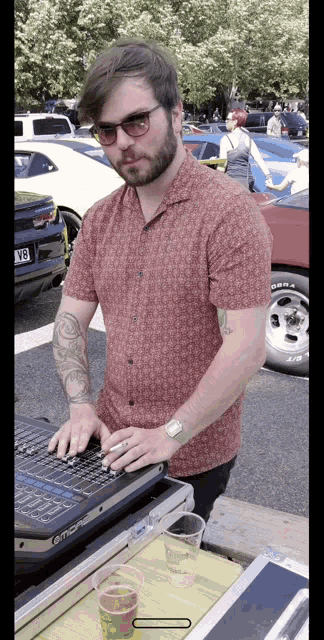 a man in a red shirt is typing on a keyboard in front of a car with the license plate v8