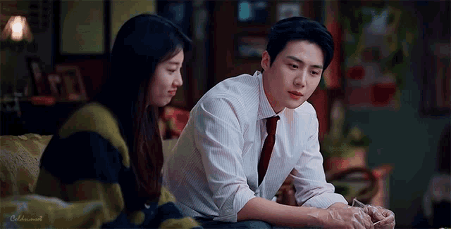 a man and a woman are sitting on a couch looking at each other . the man is wearing a tie .