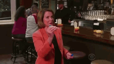 a woman in a red jacket is standing in a bar holding a cupcake .