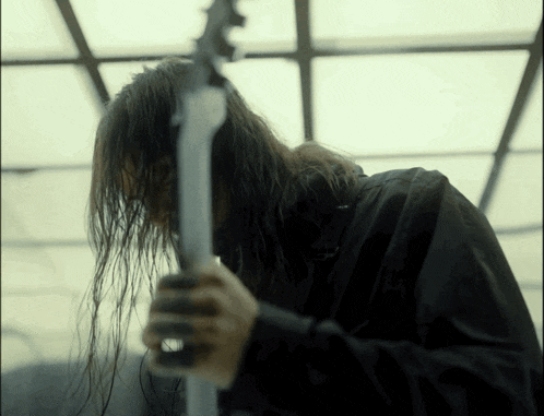 a man with long hair is playing a guitar in a dark room