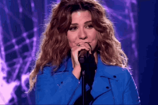 a woman singing into a microphone with a purple background