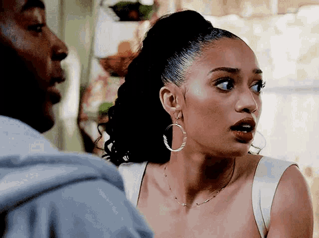a woman wearing hoop earrings is talking to a man in a room .