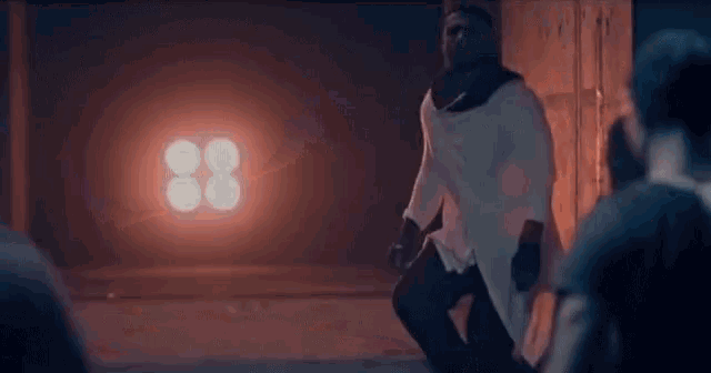 a man in a white shirt is kneeling down in front of a red light with the number 88 on it .