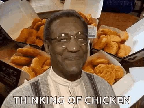 a man with glasses is standing in front of boxes of fried chicken and says thinking of chicken .
