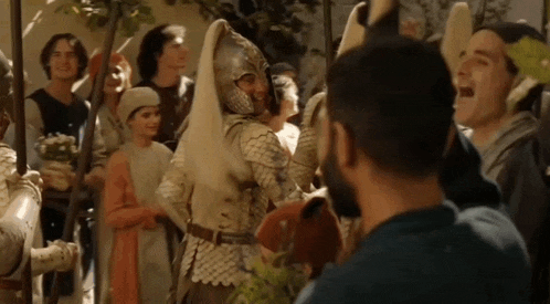 a man in a blue shirt is standing in front of a crowd of people in armor