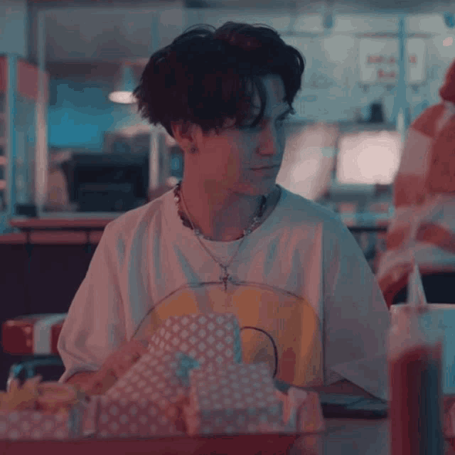 a young man wearing a smiley face shirt sits at a table with a tray of food
