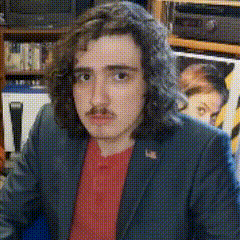 a man with long hair and a red shirt is wearing a blue suit