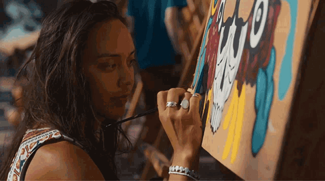 a woman with a ring on her finger is painting a picture on an easel