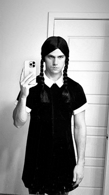 a man in a black dress is taking a selfie with his phone .
