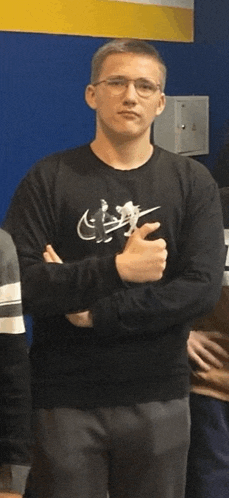 a man wearing glasses and a black nike sweatshirt stands with his arms crossed