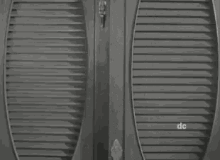 a black and white photo of a person opening a door with a bottle of alcohol in their hand .