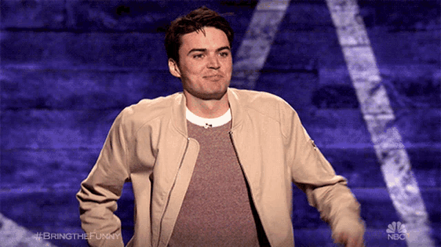 a man in a tan jacket is standing in front of a nbc advertisement