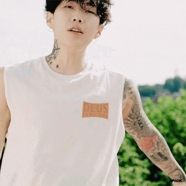 a man with a tattoo on his neck is wearing a white tank top with deus written on it