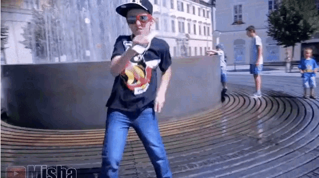 a young boy in a superman shirt is dancing in front of a fountain