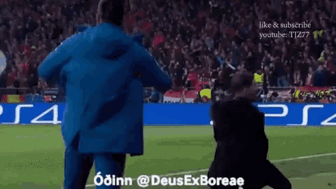 a man in a blue jacket stands on a soccer field in front of a ps4 banner