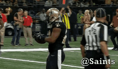 a saints football player stands on the field with a referee