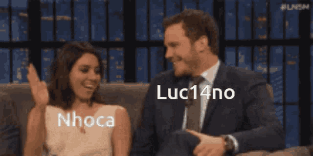 a man and a woman are sitting on a couch with their arms in the air and the words luc14no written on the screen