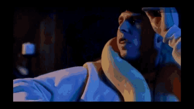 a man with a snake around his neck is in a dark room with a candle in the background .