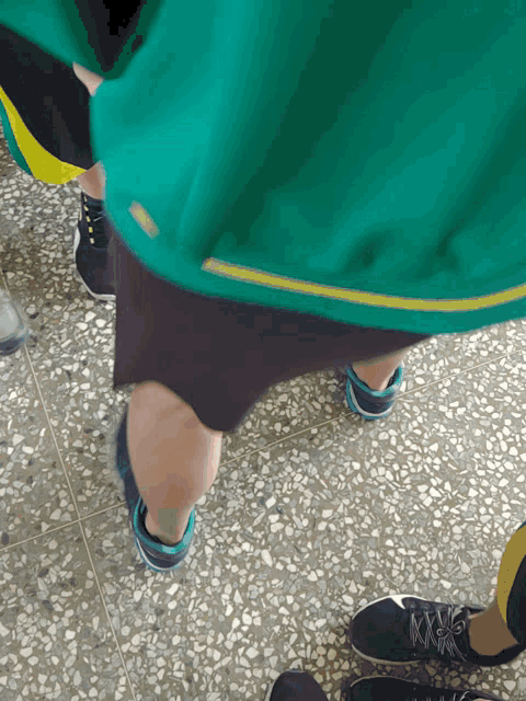 a person wearing a green shirt and black shorts stands on a tiled floor